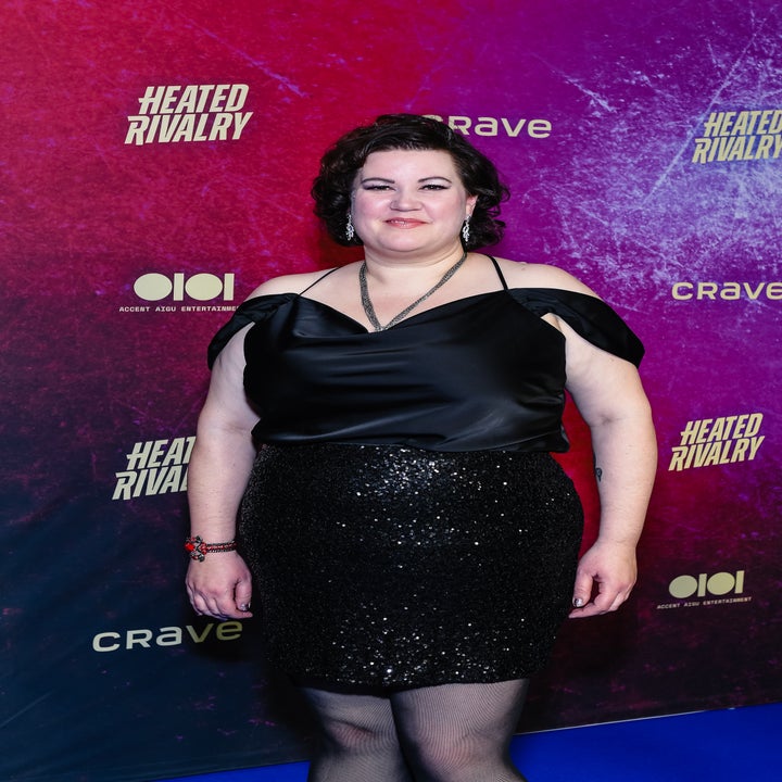 Person i en off-shoulder sateng topp og glitrende skjørt poserer på et "Heated Rivalry"-arrangement som bakteppe