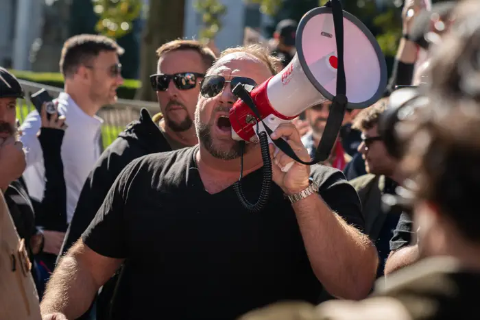 En person i en svart skjorte snakker i en megafon midt i en folkemengde utendørs under en offentlig demonstrasjon