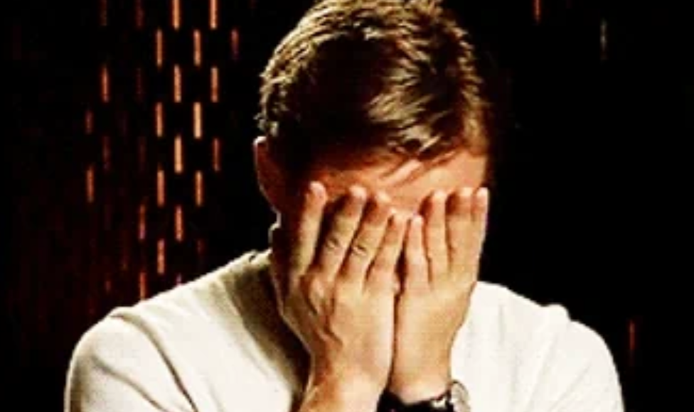 Person i uformelt antrekk som dekker ansiktet med begge hender, muligens viser følelser eller sjenanse