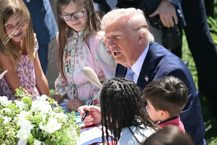 Donald Trump i dress samhandler med barn rundt et bord under et utendørsarrangement