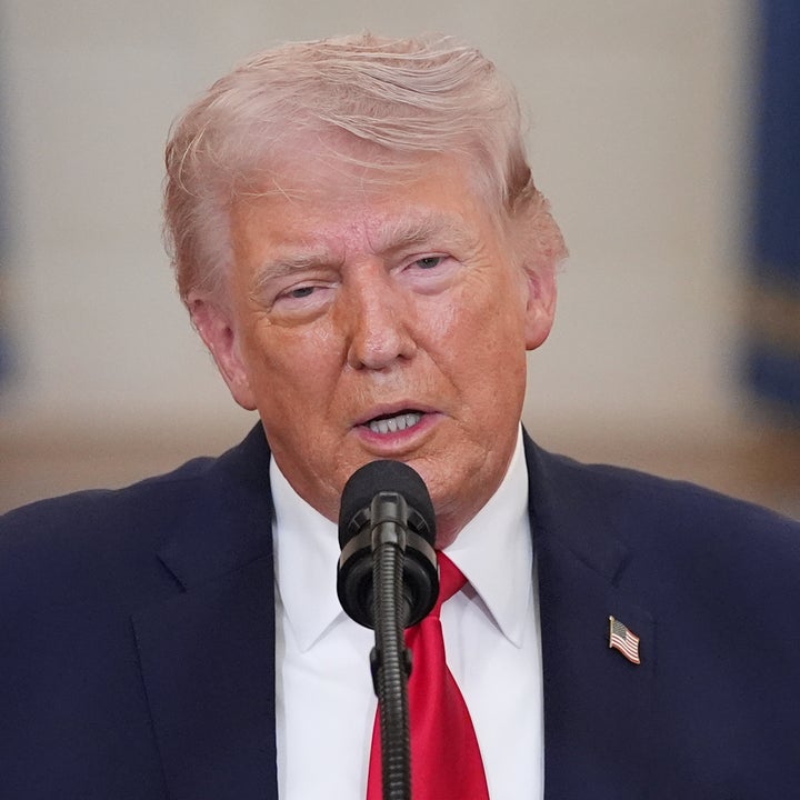 En person i dress snakker ved et podium med en mikrofon, i en innendørs setting