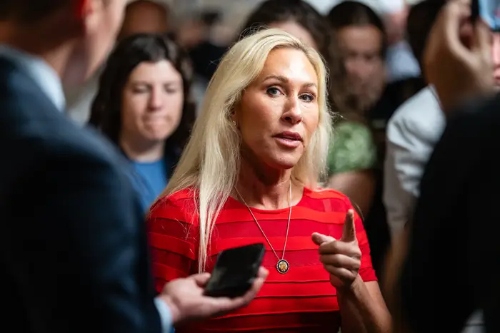 Person som snakker i overfylte omgivelser, gestikulerer med én hånd. De har langt hår og har på seg en rødstripet skjorte