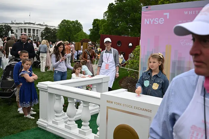 Folk som deltar på et utendørsarrangement i Det hvite hus med barn som samhandler med en utstilling med New York Stock Exchange-tema