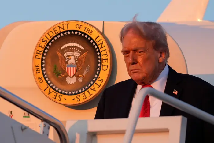 Donald Trump i dress stiger ned fra et fly med USAs presidentsegl synlig i bakgrunnen