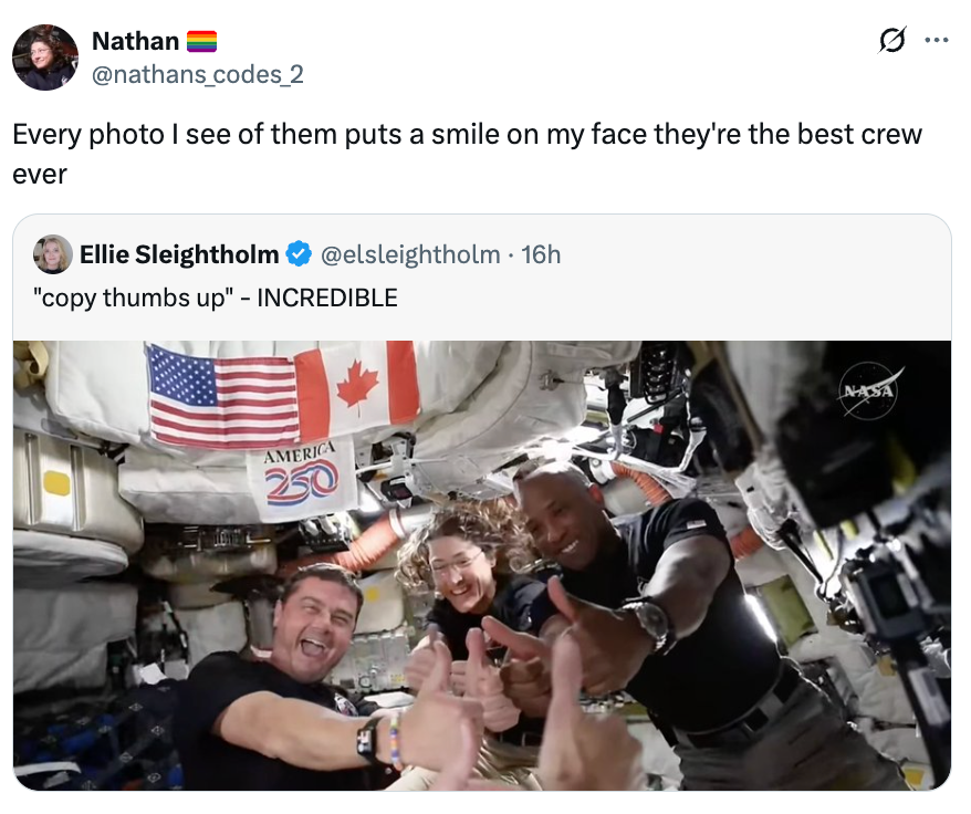 Astronauter som smiler og gir tommelen opp inne i et romfartøy, omgitt av utstyr og flagg