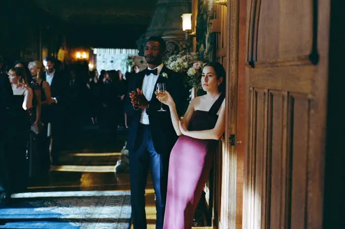 En mann i smoking og en kvinne i en elegant kjole, holder en cocktail, står på en formell begivenhet