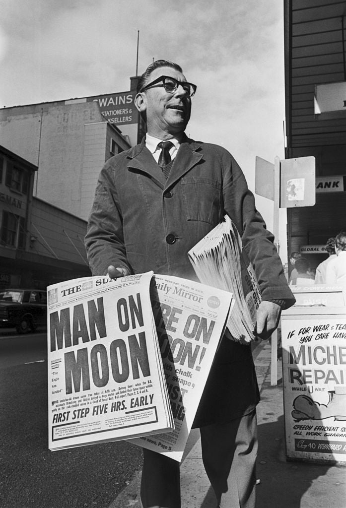 En avisleverandør holder aviser med dristige overskrifter om månelandingen, noe som indikerer begeistring for denne historiske begivenheten