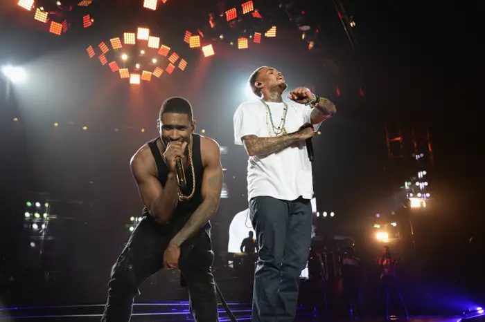 To artister på scenen, den ene iført en ermeløs topp og kjeder, den andre i en hvit t-skjorte og halskjeder, som engasjerer publikum energisk