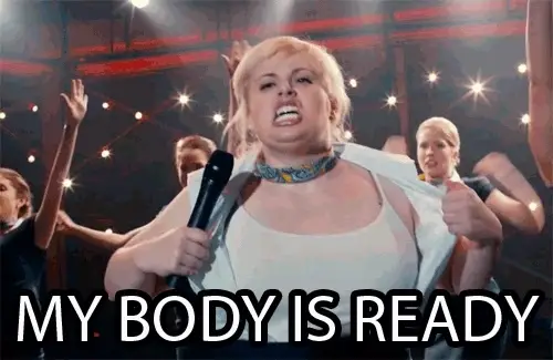 Person på scenen som på humoristisk vis river opp skjorta med et selvsikkert uttrykk, omgitt av backup-dansere. Teksten lyder: 