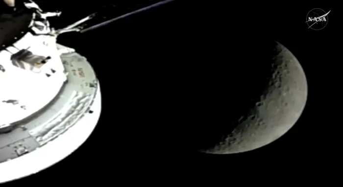 Et romfartøy nærmer seg månen, delvis synlig i en halvmånefase, med en NASA-logo i hjørnet