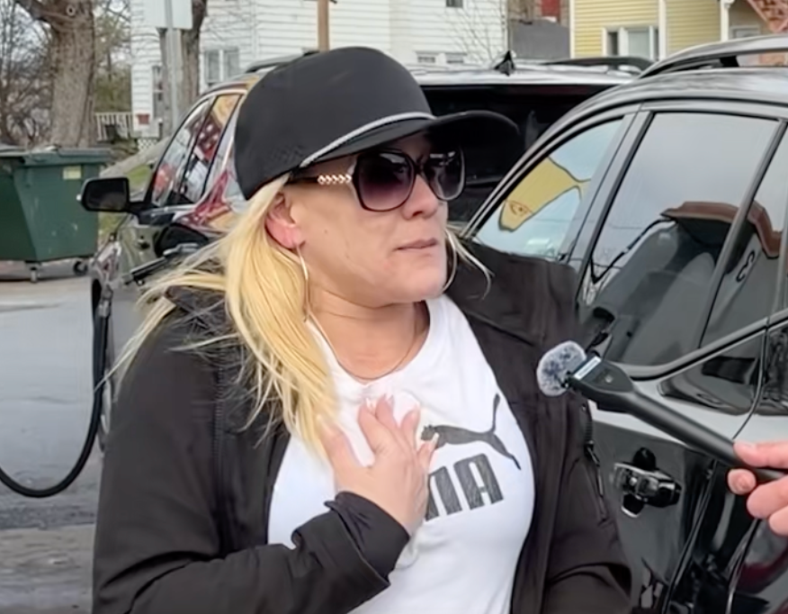 En person med solbriller og caps snakker i en mikrofon på gaten, og ser ut til å være engasjert i en samtale