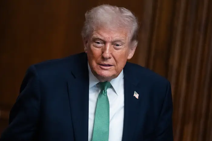 En person i dress med grønt slips er avbildet mot en trepanelbakgrunn