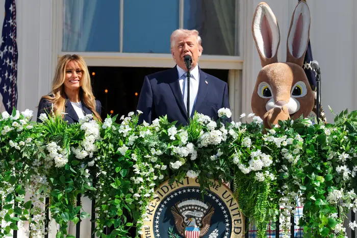 Donald Trump taler ved et podium med en presidentsegl, flankert av en kvinne i et formelt antrekk og en påskeharekarakter