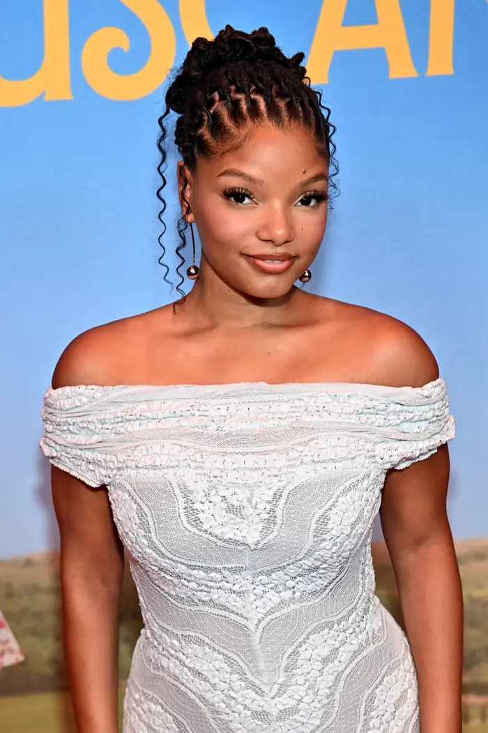 Person i en off-the-skulder blondekjole poserer på et arrangement. Bakgrunnen har stor tekst som antyder en formell anledning