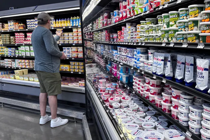 En person handler i meierigangen til en dagligvarebutikk, omgitt av forskjellige yoghurt- og rømmeprodukter