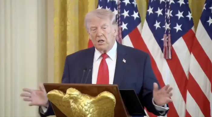 En person snakker ved et podium med et ørneemblem, foran amerikanske flagg