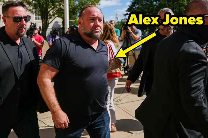 En gruppe mennesker som gikk utenfor blant journalister og kameraer, en mann i sentrum iført en svart poloskjorte, eskortert av sikkerhetsvakt