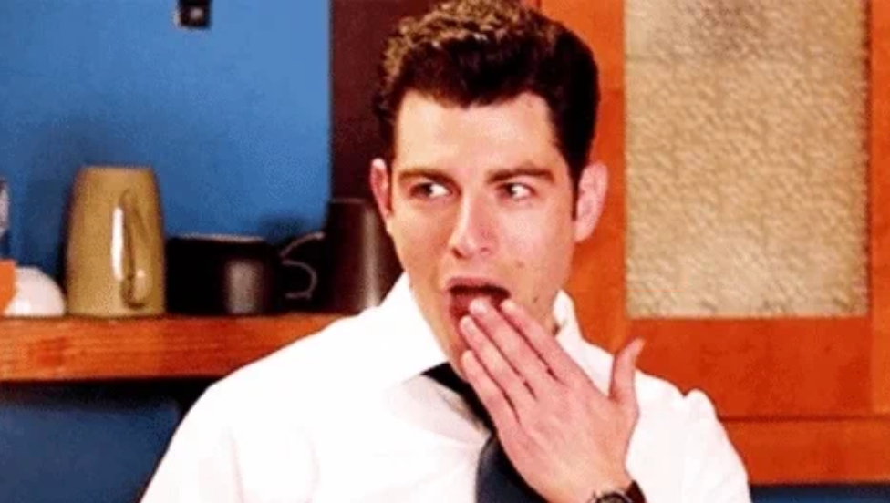 Person på et kjøkken med overrasket uttrykk, iført hvit skjorte og slips, dekker munnen med hånden