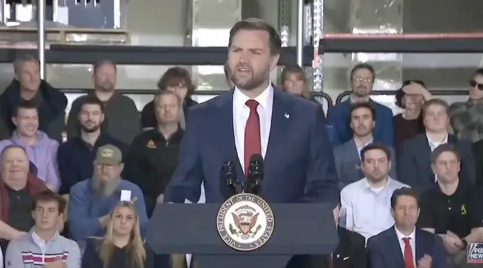 En foredragsholder står ved et podium med det amerikanske emblemet og henvender seg til et publikum i en uformell setting