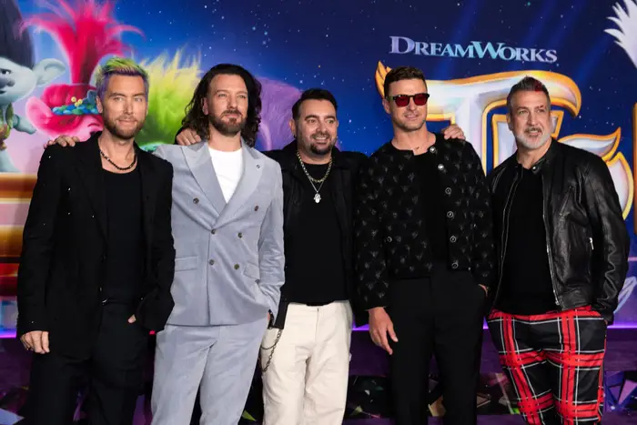 Fem personer poserer sammen på et DreamWorks-arrangement. De har på seg stilige antrekk: casual, dresser og dristige mønstrede bukser