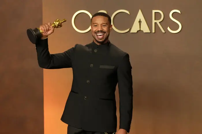 Skuespiller holder en Oscar-statue, iført en skreddersydd dress, smiler etter bilder på et arrangement