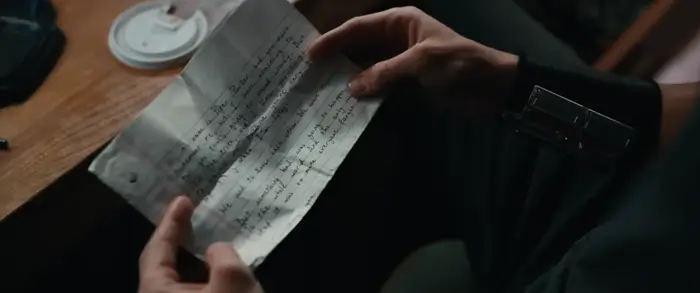 En person holder et håndskrevet brev og leser oppmerksomt ved et skrivebord