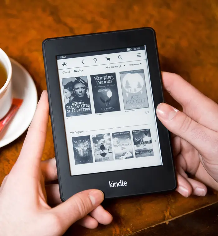 Person som holder et Kindle-visningsbokbibliotek, ved siden av en kopp te på et bord
