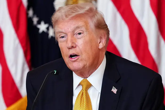 En person i dress og slips snakker på et podium foran et bakteppe med stjerner og striper