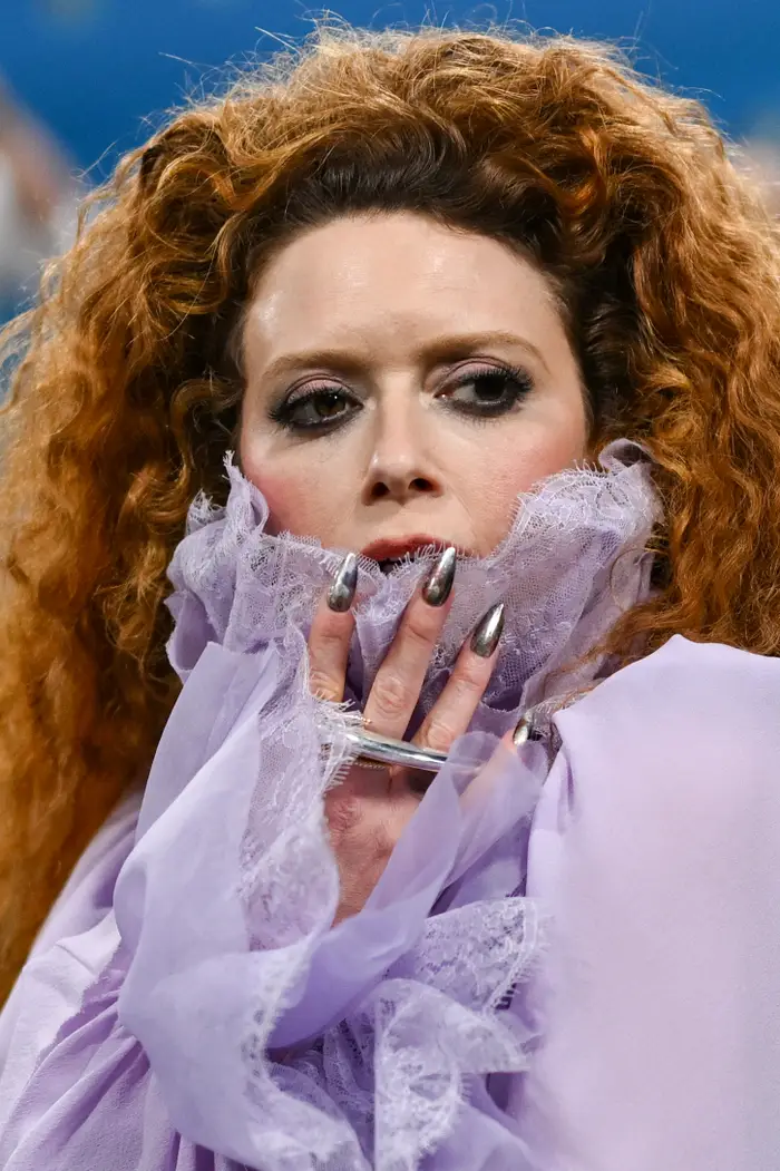 Natasha Lyonne på rød løper med voluminøst rødt hår, iført rynket, rent antrekk, dramatiske metalliske negler og dristig øyesminke