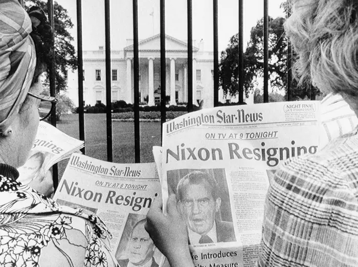 Folk som holder aviser med overskriften «Nixon Resigning»; foran portene til Det hvite hus