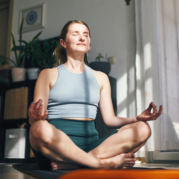 Person som mediterer fredelig på en yogamatte i en solbelyst stue, omgitt av potteplanter