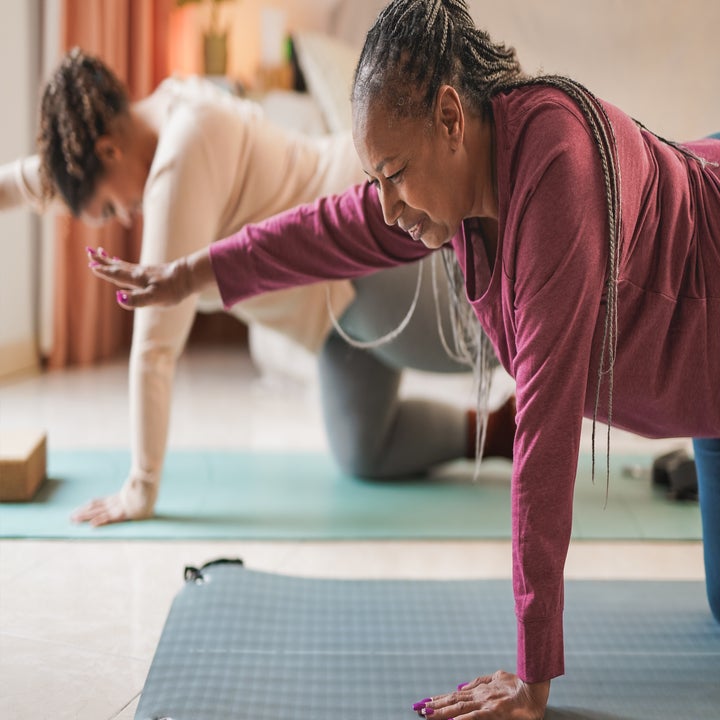 To personer som gjør yoga i en stue, begge i bordstilling med en arm strukket fremover for balanse
