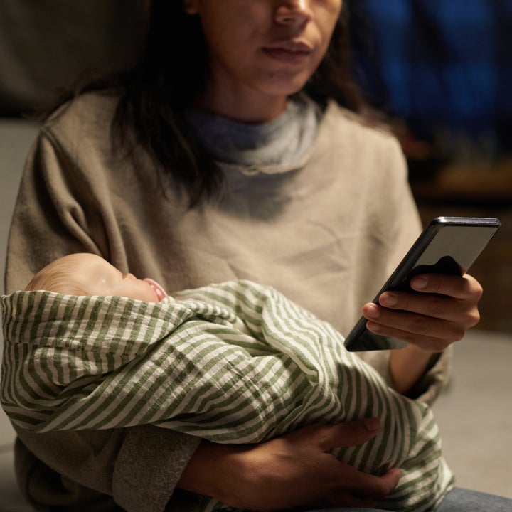 Person som vugger en sovende baby pakket inn i et rutete teppe mens han ser på en smarttelefon