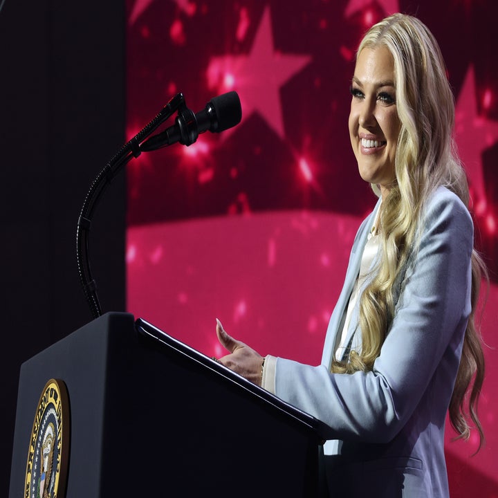 Person som snakker på et podium med en mikrofon, iført en stilig dress, med et amerikansk flagg i bakgrunnen