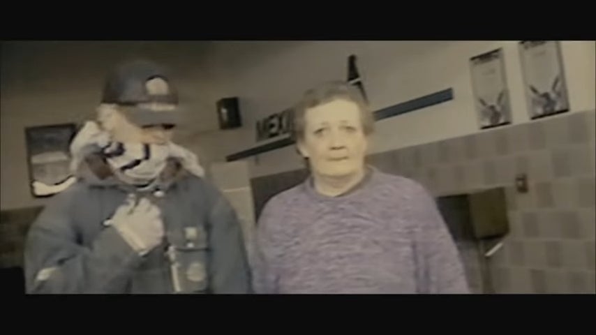 En person med hette og bandana står ved siden av en eldre kvinne inne i en bygning. Begge fremstår åpenhjertig i en uformell setting