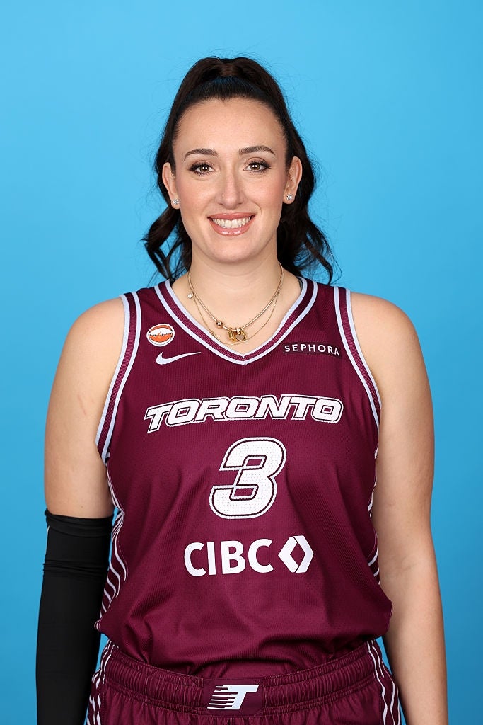 Basketballspiller i en Toronto-trøye nummer 3, smilende og iført et halskjede, med en knallblå bakgrunn