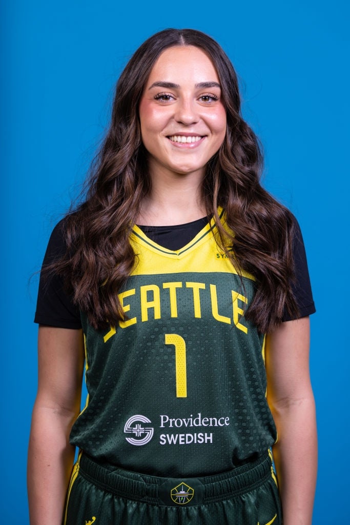 Person som smiler i en Seattle-basketballtrøye med nummer 1, stående mot en vanlig bakgrunn