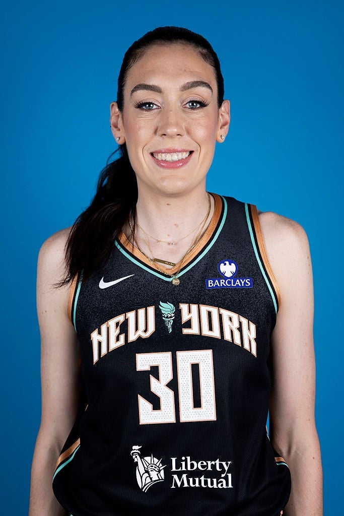 Idrettsutøver i en basketballtrøye fra New York, smilende mot en blå bakgrunn
