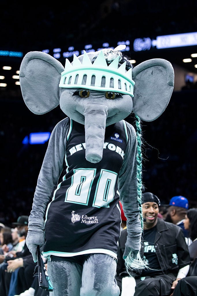 En sportsmaskot kledd som en stilisert elefant med en basketballtrøye og en kronelignende hodeplagg på et innendørs sportsarrangement