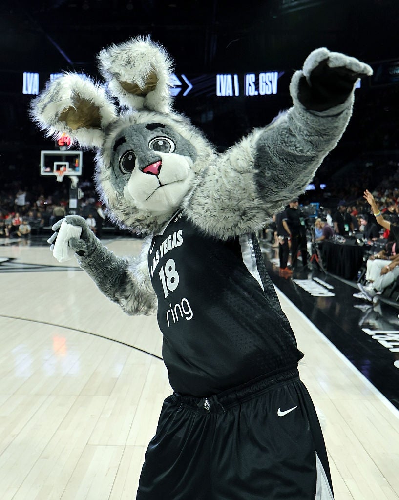 En basketballmaskot i et kanindrakt poserer energisk på banen, iført en trøye med tallet 18