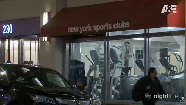 Et utvendig treningsstudio fra New York Sports Clubs med synlige treningsapparater inni. En person går på fortauet, og en bil står parkert i nærheten