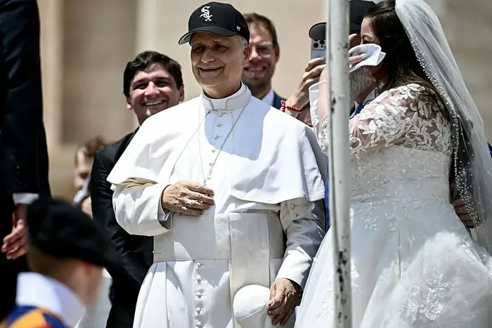 En mann i religiøs antrekk, smilende, bærer en baseballcaps. Han står sammen med et brudepar og deler et letthjertet øyeblikk