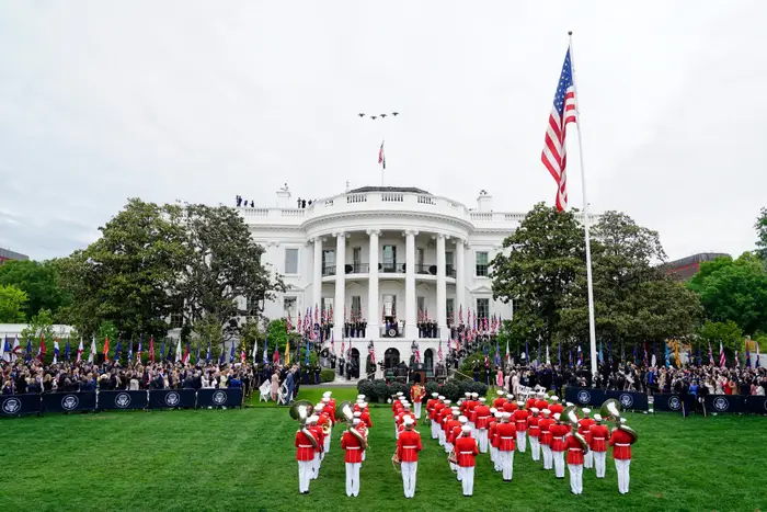 Et militærkorps opptrer på plenen foran en stor hvit bygning med søyler og et amerikansk flagg som vaier fremtredende