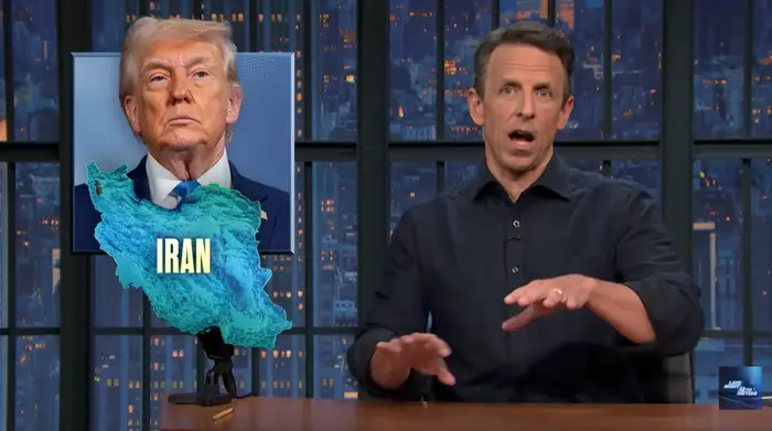 En TV-vert gestikulerer mens han diskuterer et politisk tema med et bilde av en offentlig person og Iran-kart