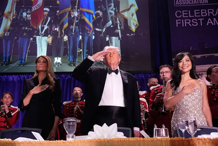 En formell begivenhet med gjester som hilser og poserer; en mann i smoking mellom to kvinner i elegante aftenkjoler