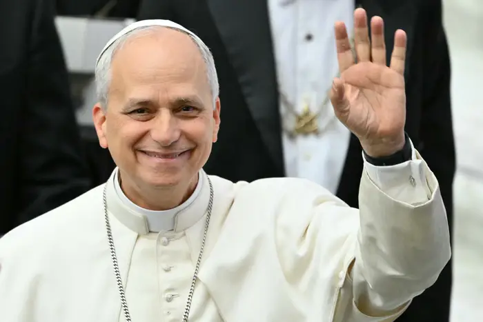 En person i religiøs antrekk vinker og smiler til kameraet, og dukker opp i en formell, seremoniell setting