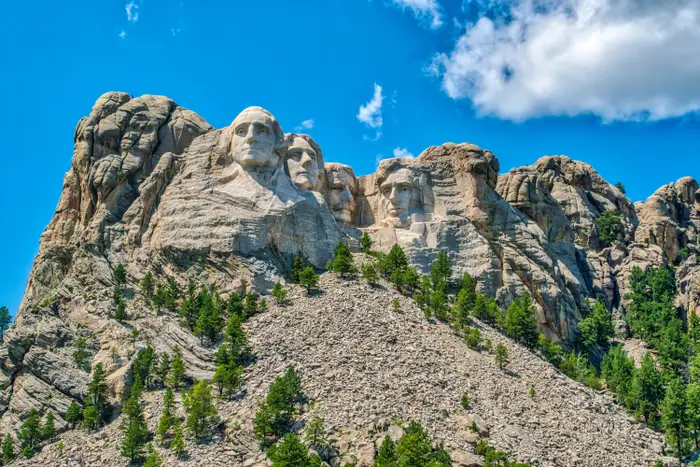 Mount Rushmore med utskårne ansikter av fire amerikanske presidenter mot et steinete landskap og delvis overskyet himmel