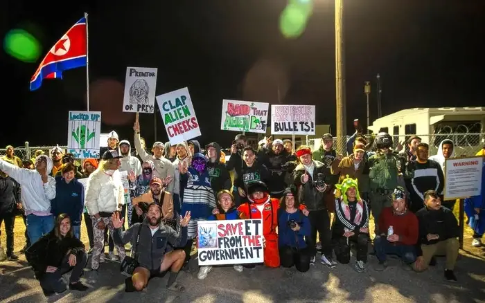 En gruppe mennesker poserer med humoristiske pro-alien-protestskilt nær Area 51 om natten