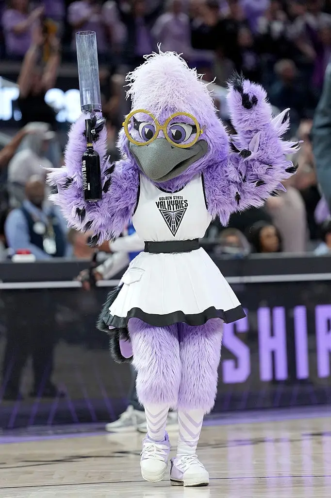 En maskot for et idrettslag i cheerleader-antrekk opptrer på en basketballbane og gir energi til publikum under en kamp