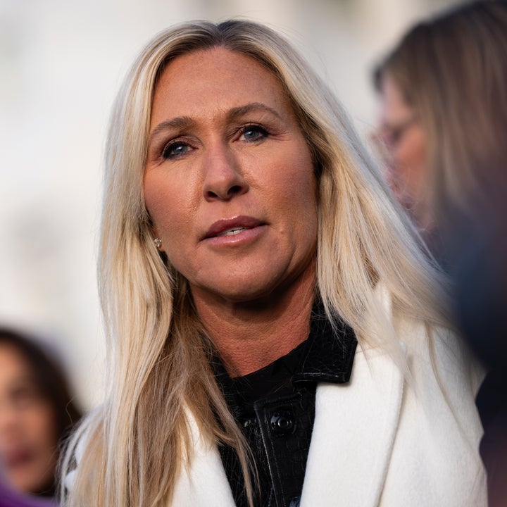 En person med langt hår og hvit frakk står blant andre utendørs og gleder seg